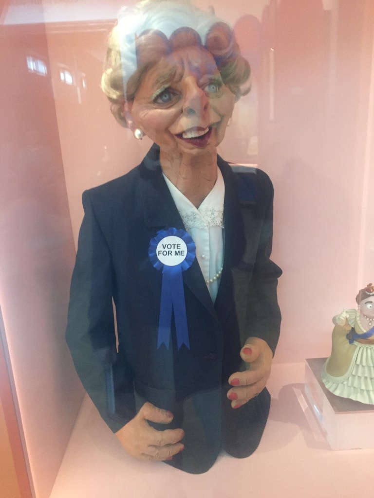 Large puppet of Margaret Thatcher, from the Spitting Image TV series. Consisting of just her head and upper body, she has slightly exaggerated facial features, while wearing a navy jacket over a white blouse, and a round ribbon attached to her jacket that says Vote For Me.