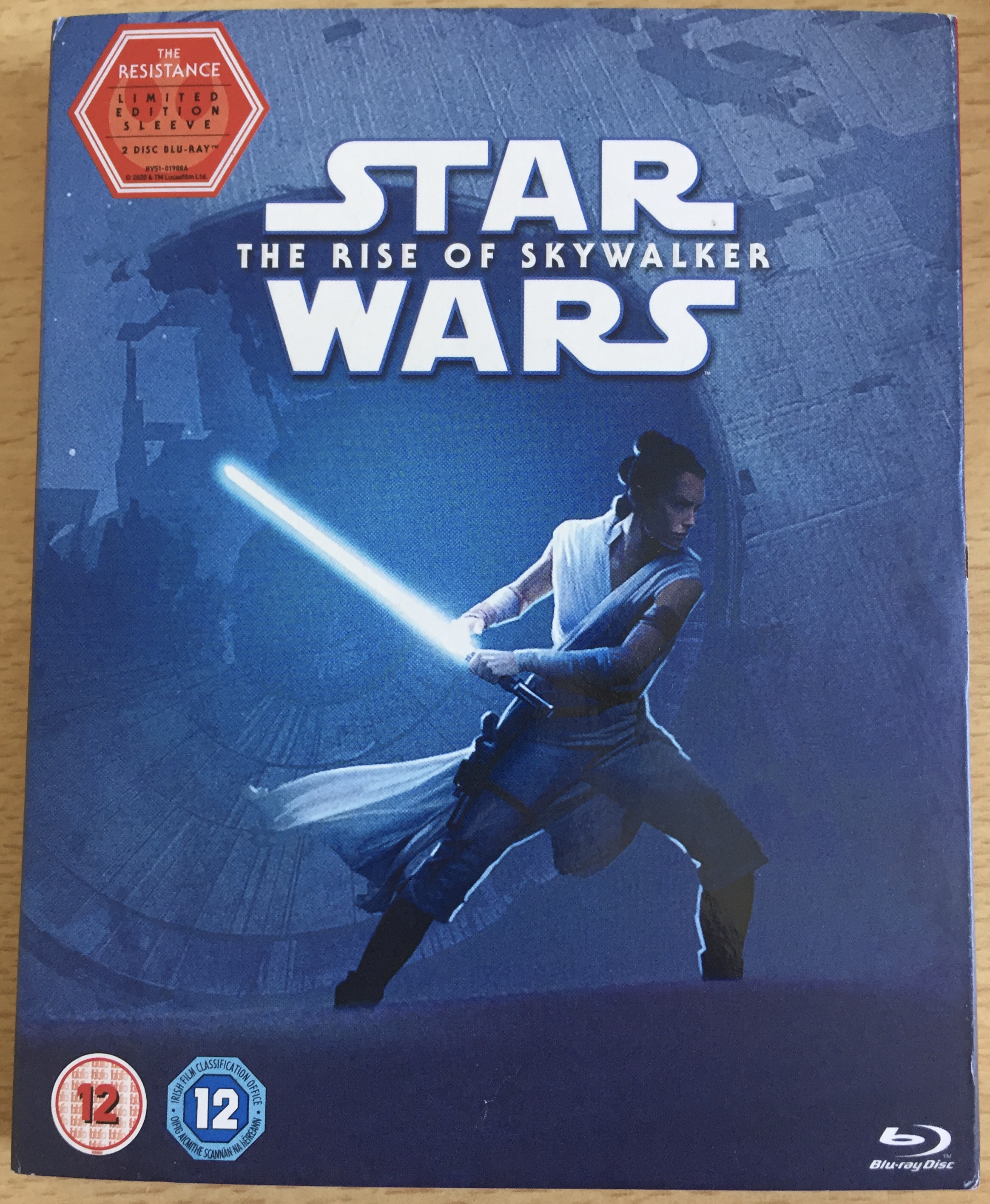 Blu-ray front cover for Star Wars Episode 9, The Rise Of Skywalker, showing Rey against a blue background, in an attack pose as she prepares to swing her lightsaber.