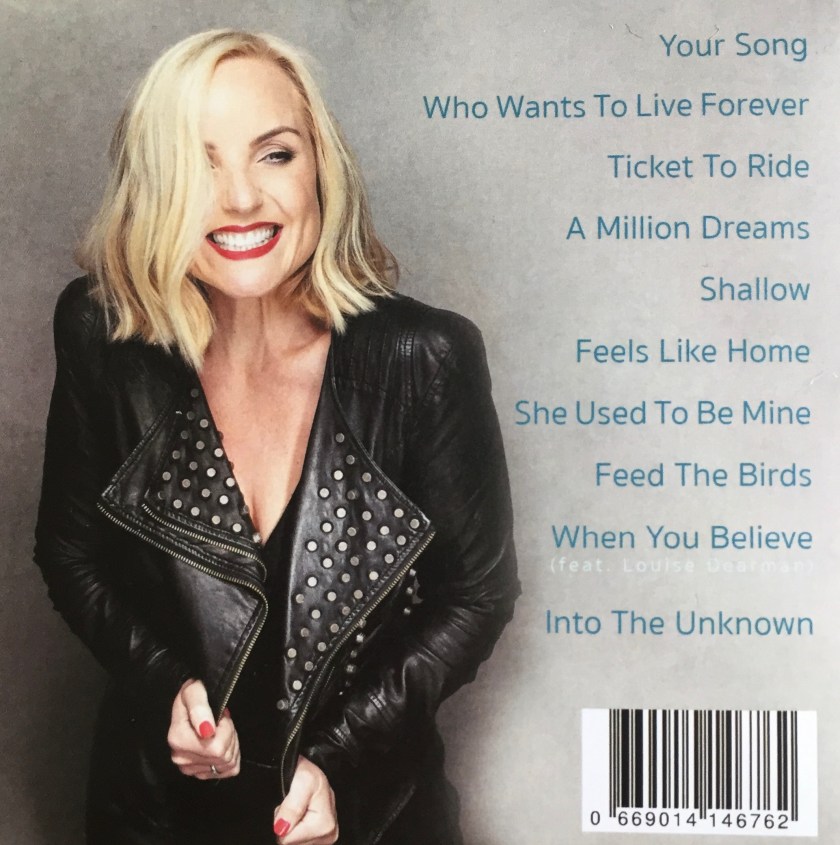 Back cover of the Kerry Ellis album Feels Like Home To the left of the list of tracks, Kerry is grinning widely as she partially holds open her black leather jacket, revealing lots of metal studs lining the inside.