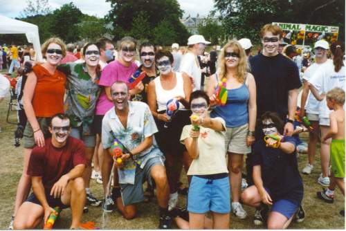 A smiling team of 10 people, including Glen, their faces painted in white, with black across the eyes, and all holding water pistols.