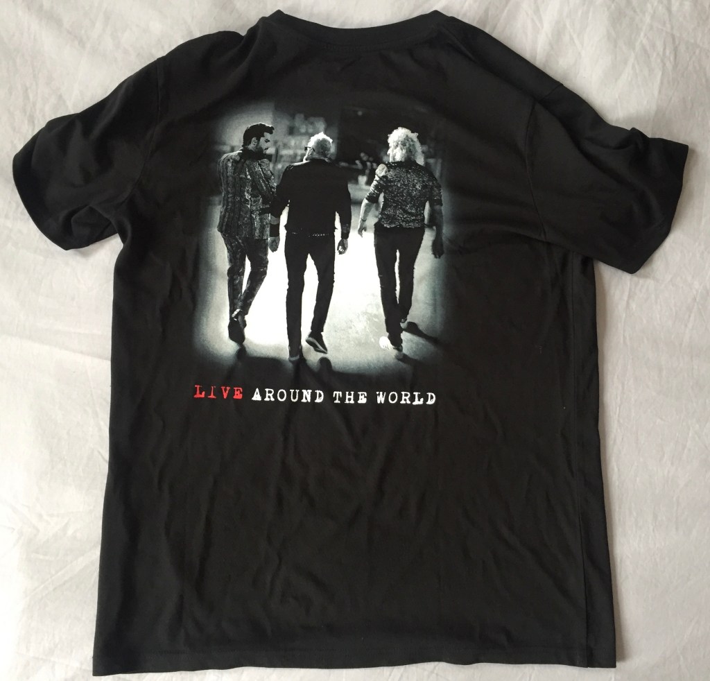 Black t-shirt featuring a black and white image of Adam Lambert, Roger Taylor and Brian May glancing at each other as they walk off towards the stage. Text below the photos says Live Around The World, with the word Live in red, and the other words in white.