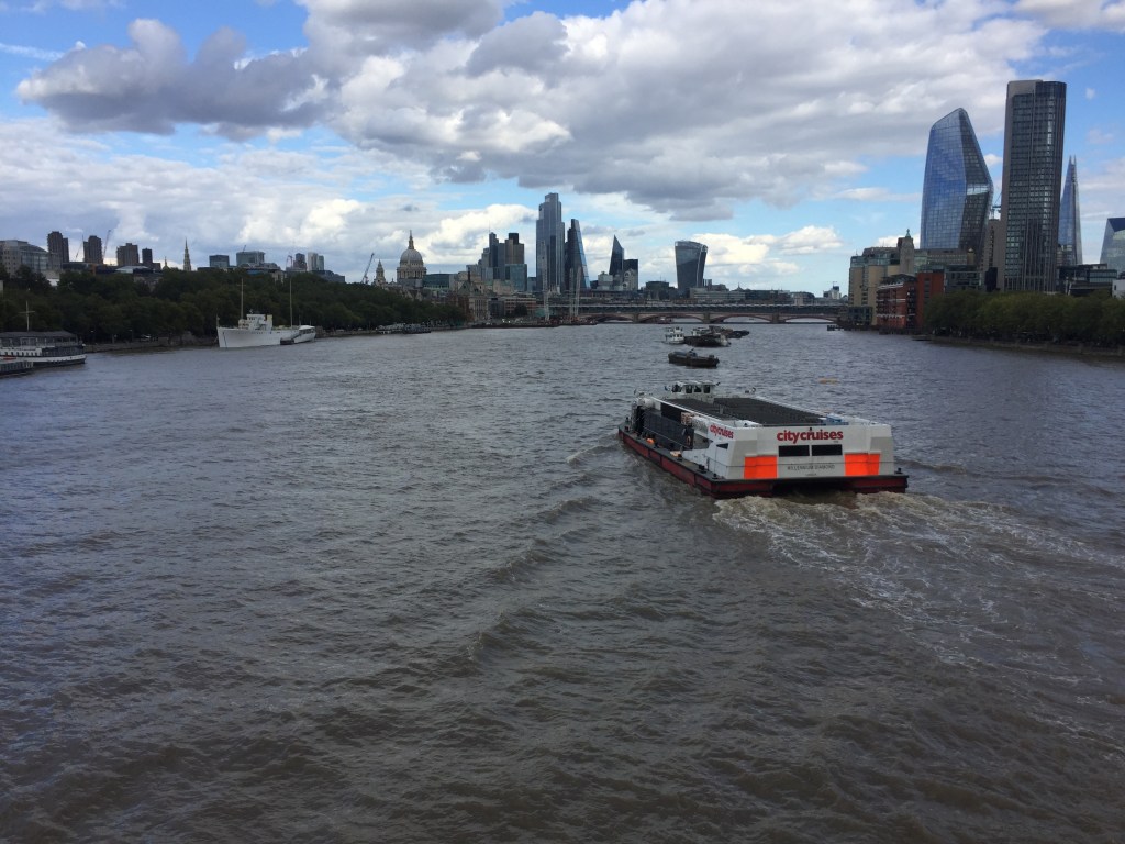 A City Cruises boat, with completely empty seats on the top deck, sailing down the Thames.