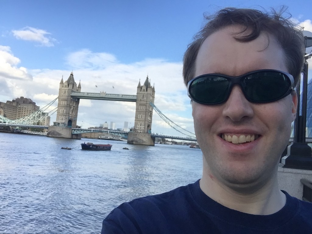 Selfie of Glen smiling and wearing dark glasses in front of Tower Bridge.