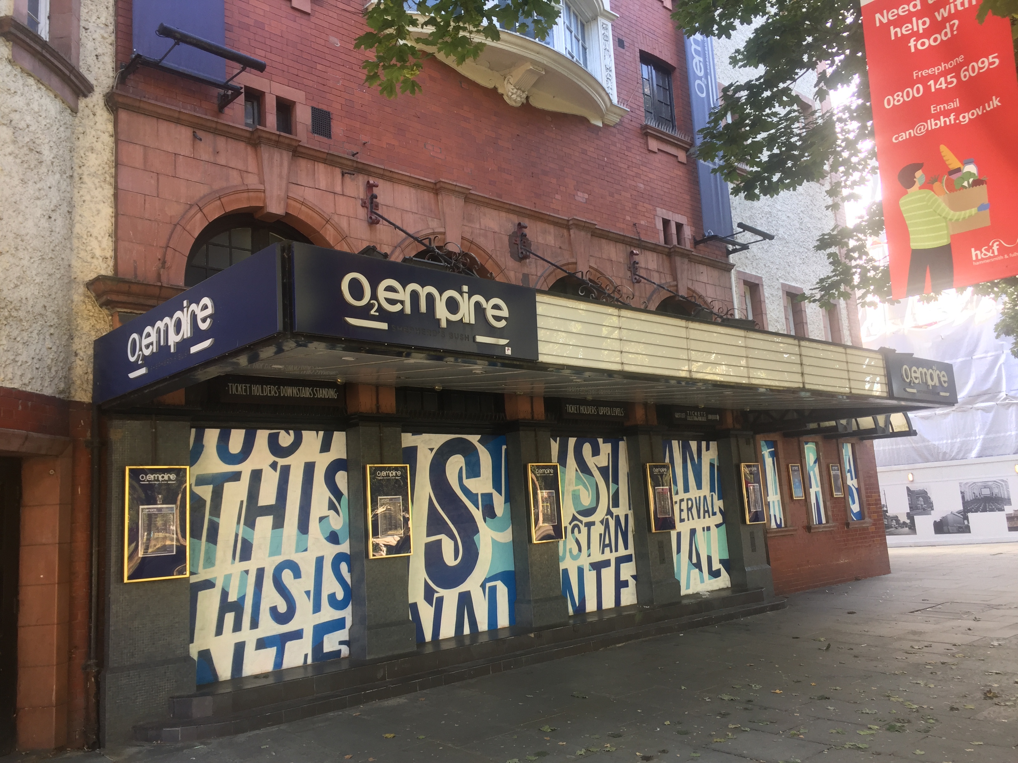 The front of the Shepherd's Bush Empire, now called the O2 Empire. White posters cover up the 4 windows along the front, with stylistic blue lettering that reads This Is Just An Interval, in reference to the shutdown enforced by the Covid pandemic.