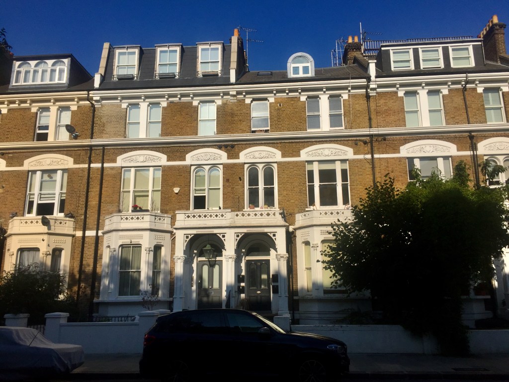 A row of 3 storey terraced houses in traditional brickwork with white framed windows. Most of them have a roof extension on top with windows going across, but one of them, number 36, has just a tiny arched window sticking up in the centre of its roof.