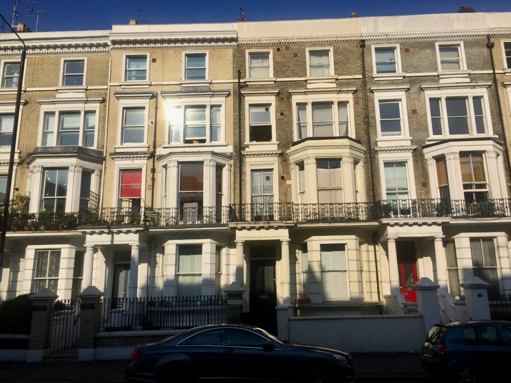 A row of 4 storey terraced houses, in traditional brickwork with white framed windows and a flat roof.