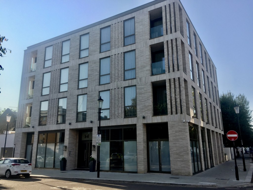 A tall, grey, 4 storey building on a street corner, with equally spaced vertical windows on each floor, and very narrow slitted windows on the corners of the upper 3 floors.