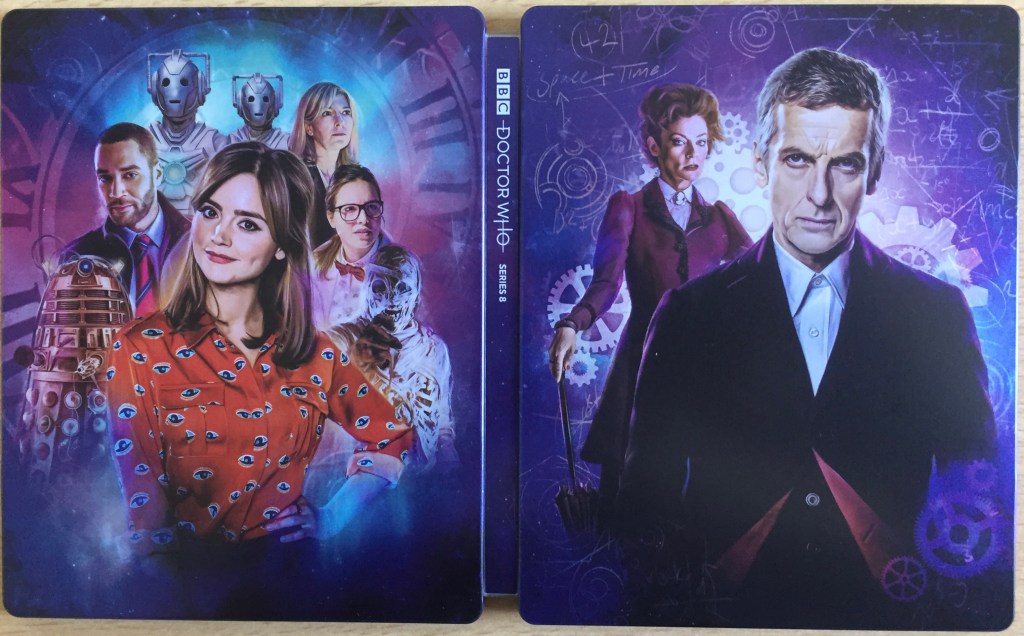 Steelbook cover for the Doctor Who Series 8 Blu-ray, showing Peter Capaldi's Doctor with Clara, Missy, the Cybermen and other characters from the series, against a dark blue background decorated with cogs, bubbles, and a large clock face.