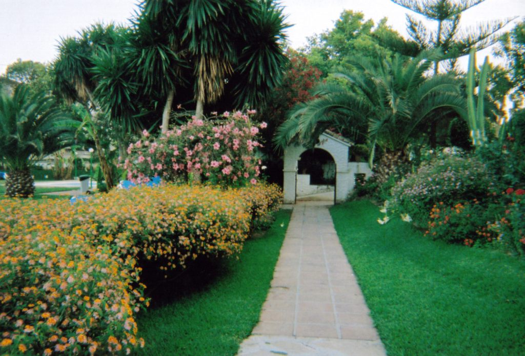 A path leading to a white archway, with greenery and colourful flowered bushes on each side, at Carihuela Park Palace.