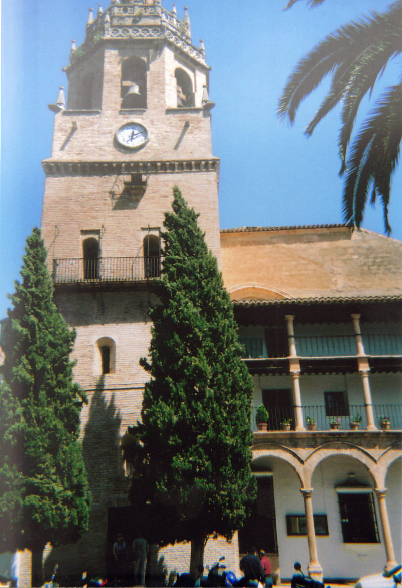 Church of Santa Maria La Mayor in Ronda. A tall bell tower, with a small clock just below the bell, is connected to a smaller three-storey structure with arches along the lower floor.