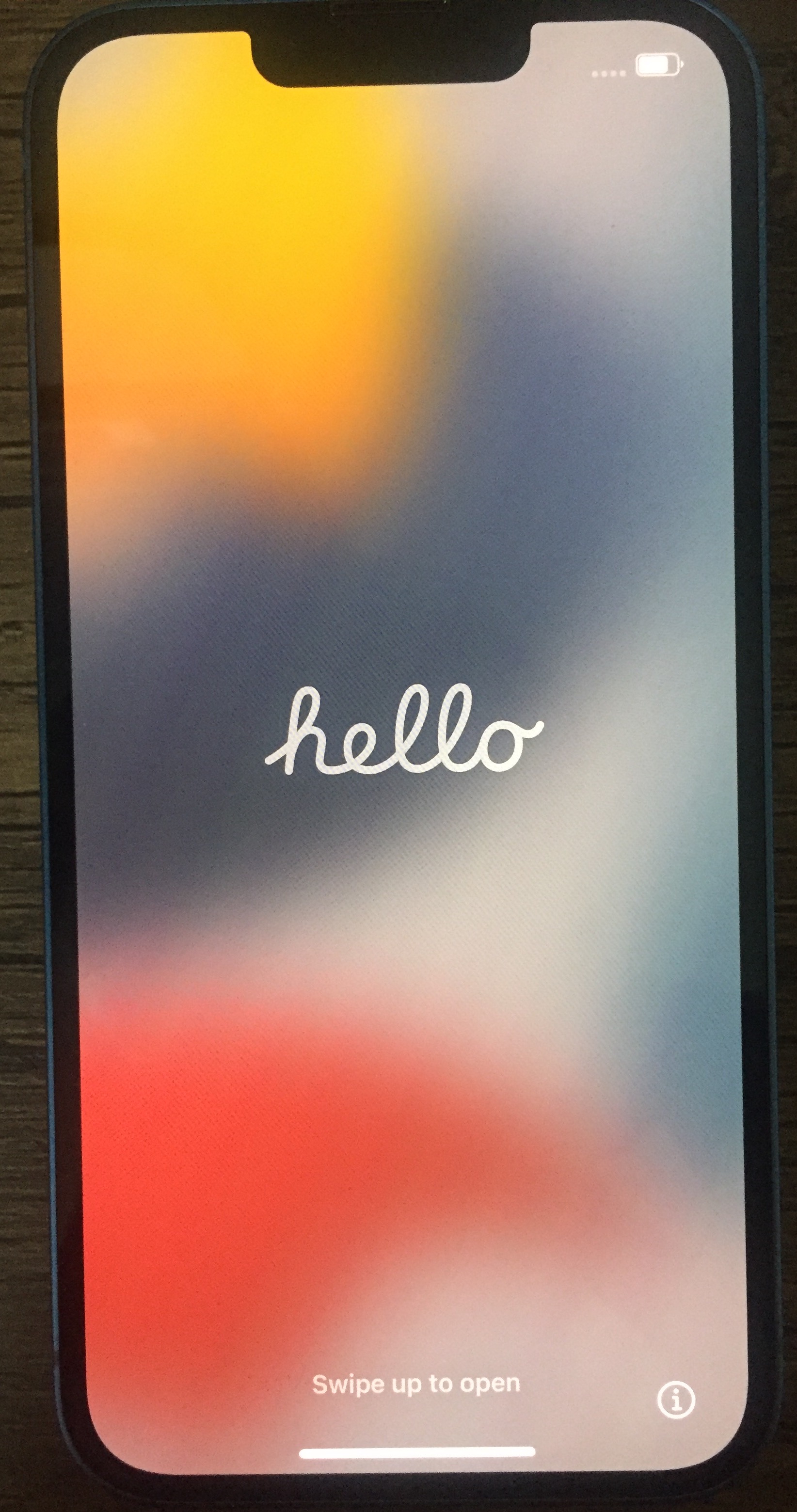 iPhone 13 showing the welcome screen. Over a blurry multi-coloured background, clear white text in a curly phone says hello. Small white text at the very bottom says swipe up to open.