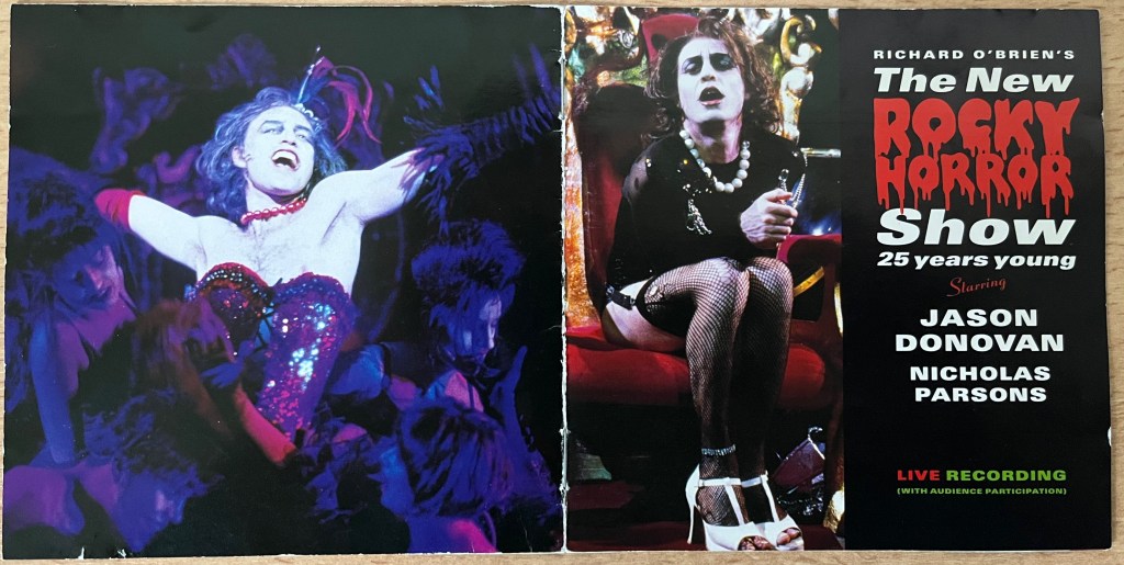 CD booklet cover spread from the 1998 live Rocky Horror album, showing Jason Donovan as Frank N. Furter on the front and back covers. On the front he's seated, wearing a black top, white pearl necklace, black fishnets and white heels. On the back he's wearing a sparkly corset as he dances proudly.