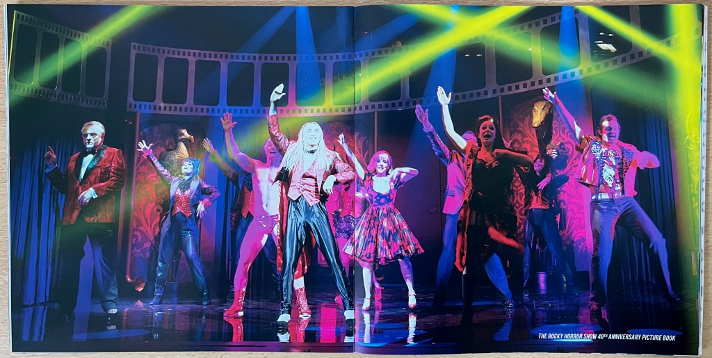 Double-page spread from the Rocky Horror 40th anniversary photo book, with Riff Raff leading the cast in the Time Warp as they raise their right hands in the air.