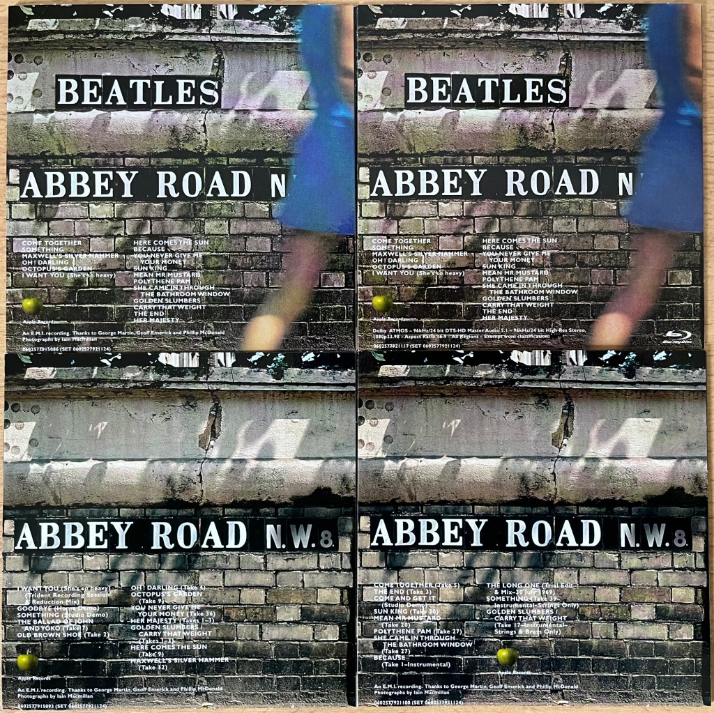 Back covers of the disc sleeves from the Abbey Road box set, all showing the track listing against a brick wall with the Abbey Road sign on it. 2 of the sleeves also have an additional sign higher up the wall saying Beatles, and the blurry figure of a leg and the lower edge of a skirt as a lady walks past on the right.