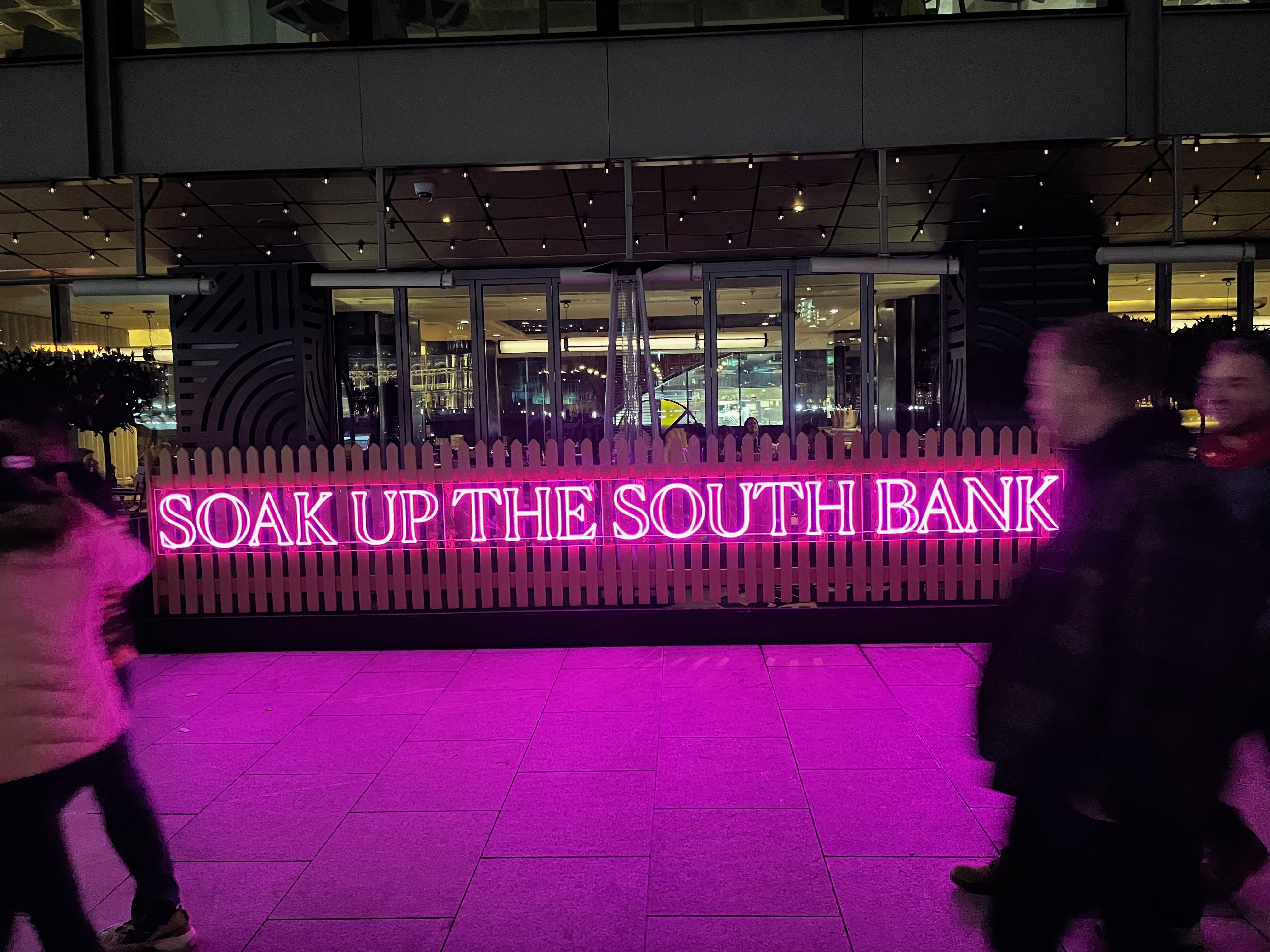 Wall sign saying Soak Up The South Bank in large capital letters lit up in pink.