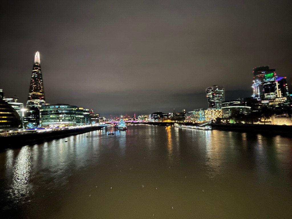 View west along the Thames from Tower Bridge, including the Shard lit up and towering tall above the buildings on the left, and the Walkie Talkie building further along on the opposite bank.