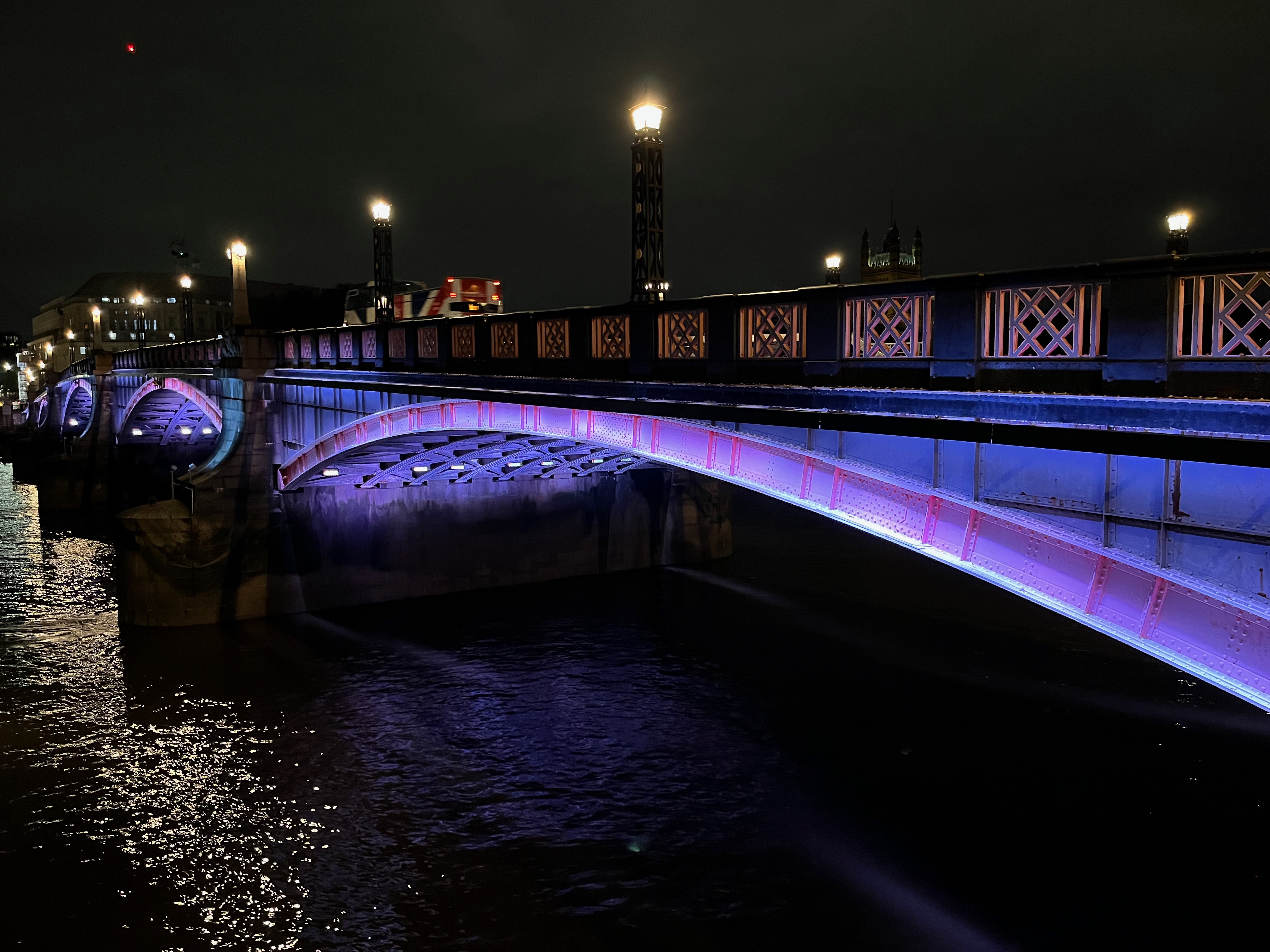 Close-up of an arch on Lambeth Bridge, lit up in blue beneath ornate railings.