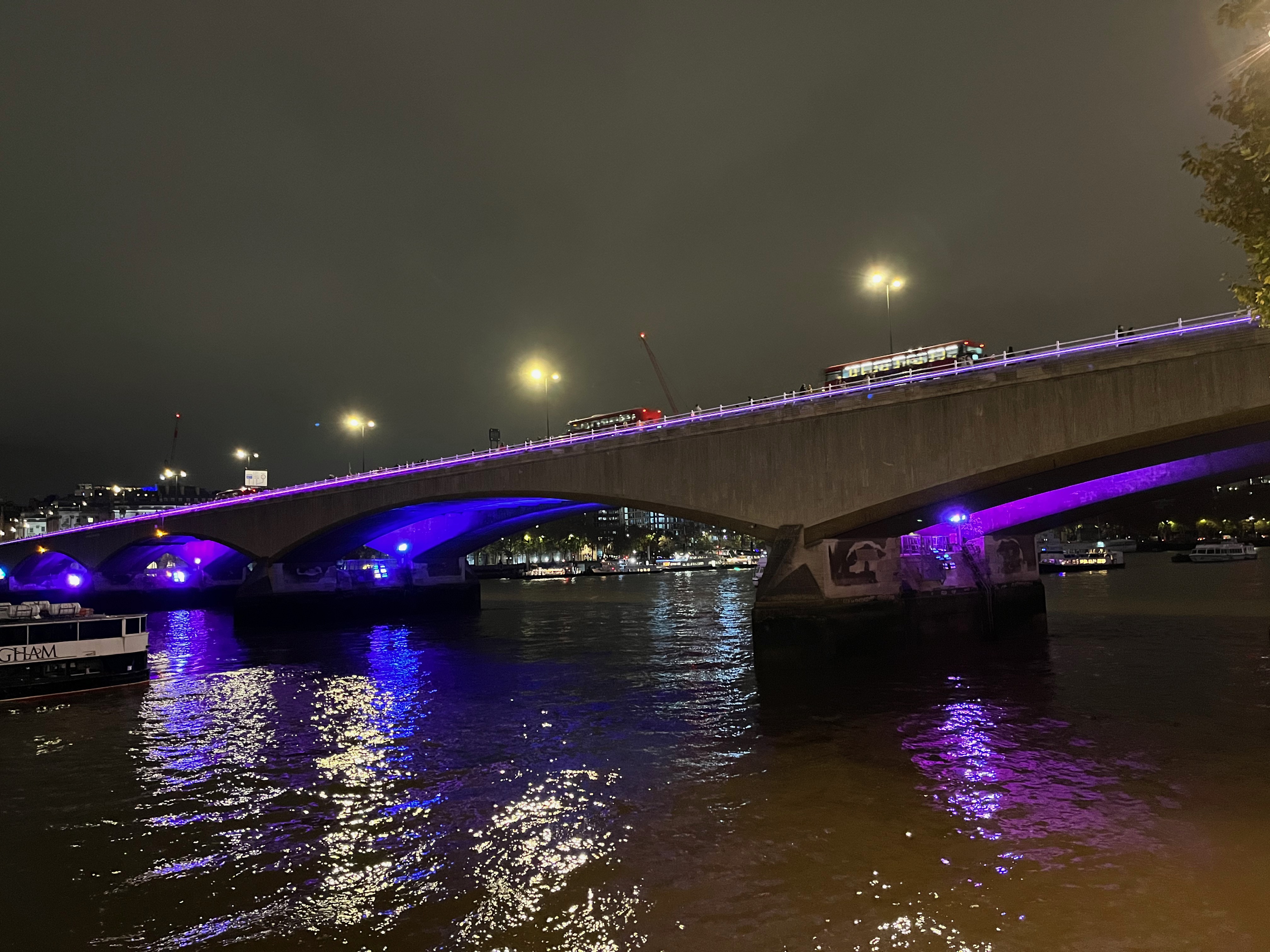 Waterloo Bridge, with alternating blue and purple light bathing the underside of its 4 wide arches, and a thin line of pink light along the top of the bridge.