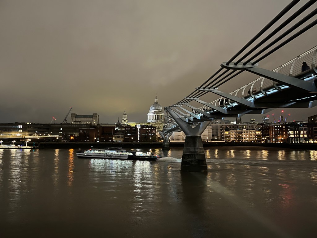 Close-up view of the Millennium Bridge, viewed towards St Paul's Cathedral on the opposite bank, as an Uber boat passes under the bridge.