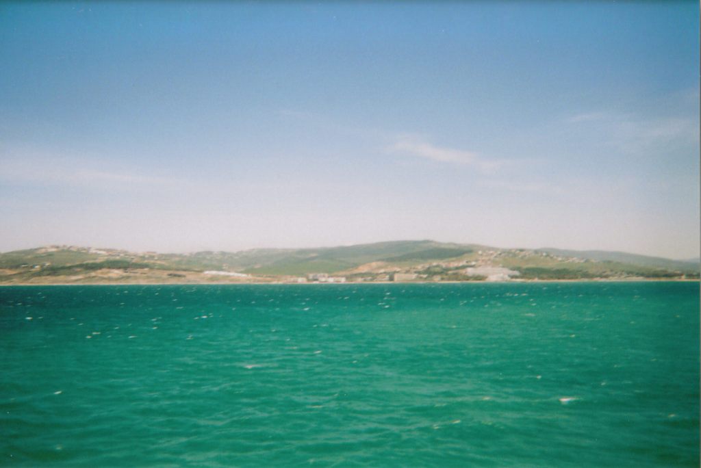 View from a boat towards a shoreline with a green hilly landscape.