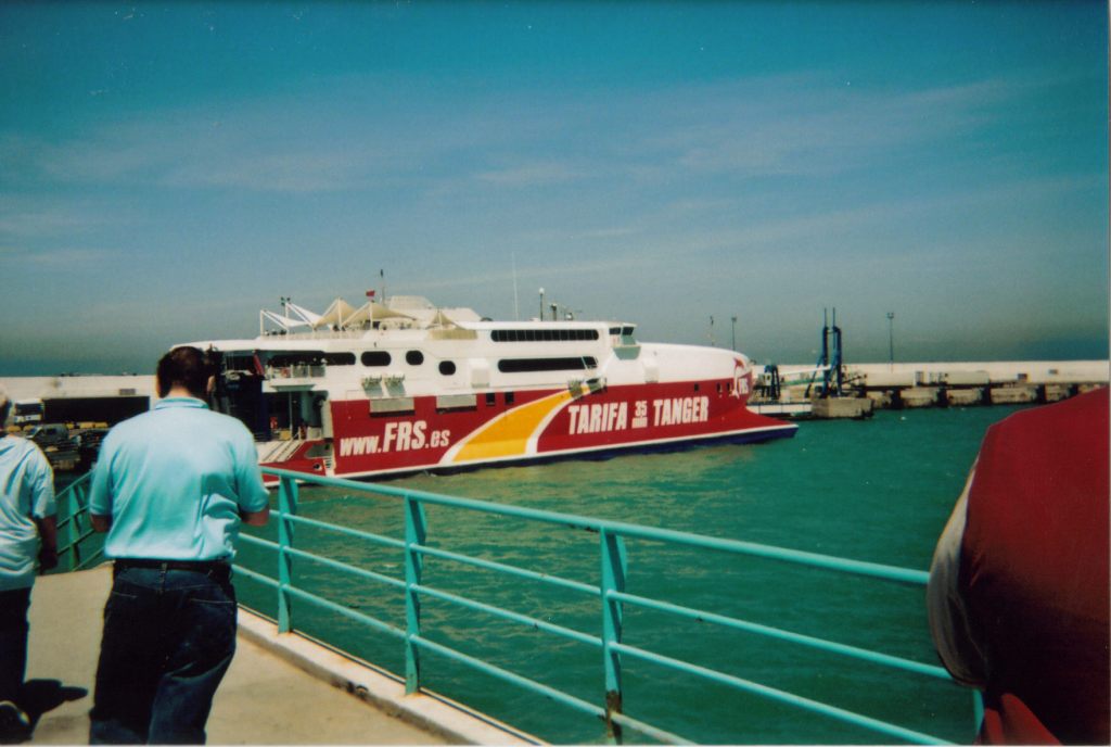 The boat that brought us to Tangier. The white upper section of the boat has 2 long windows one above the other for each passenger deck. Below that, the large red hull that holds the car deck has large white lettering that says Tarifa Tanger, and gives the website address www.frs.es