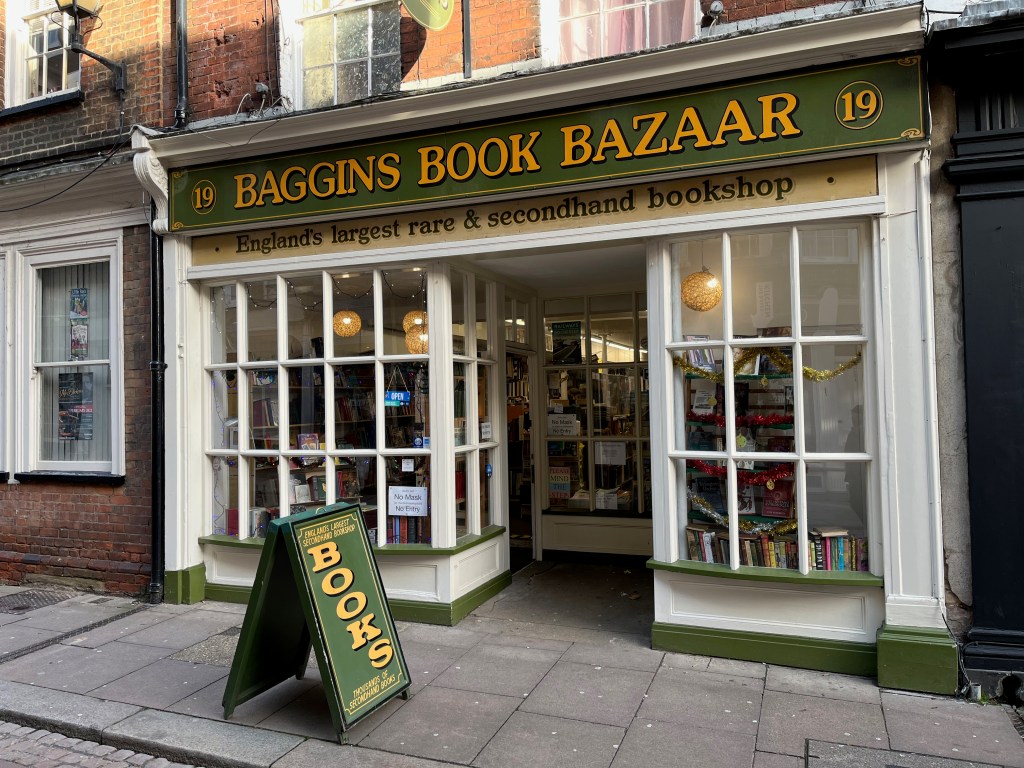 The exterior of Baggins Book Bazaar, England's largest rare and secondhand bookshop. The name is printed in gold lettering on a green background above the shop, while a green A-board on the pavement has the word Books in large gold letters.