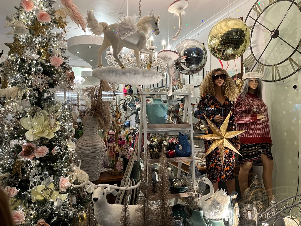 Window display for the Kiss Kiss Heart shop, full of pretty and shiny objects and decorations, including silver and gold mirror balls, a white horse, a white reindeer, a gold star, and a heavily decorated Christmas tree.