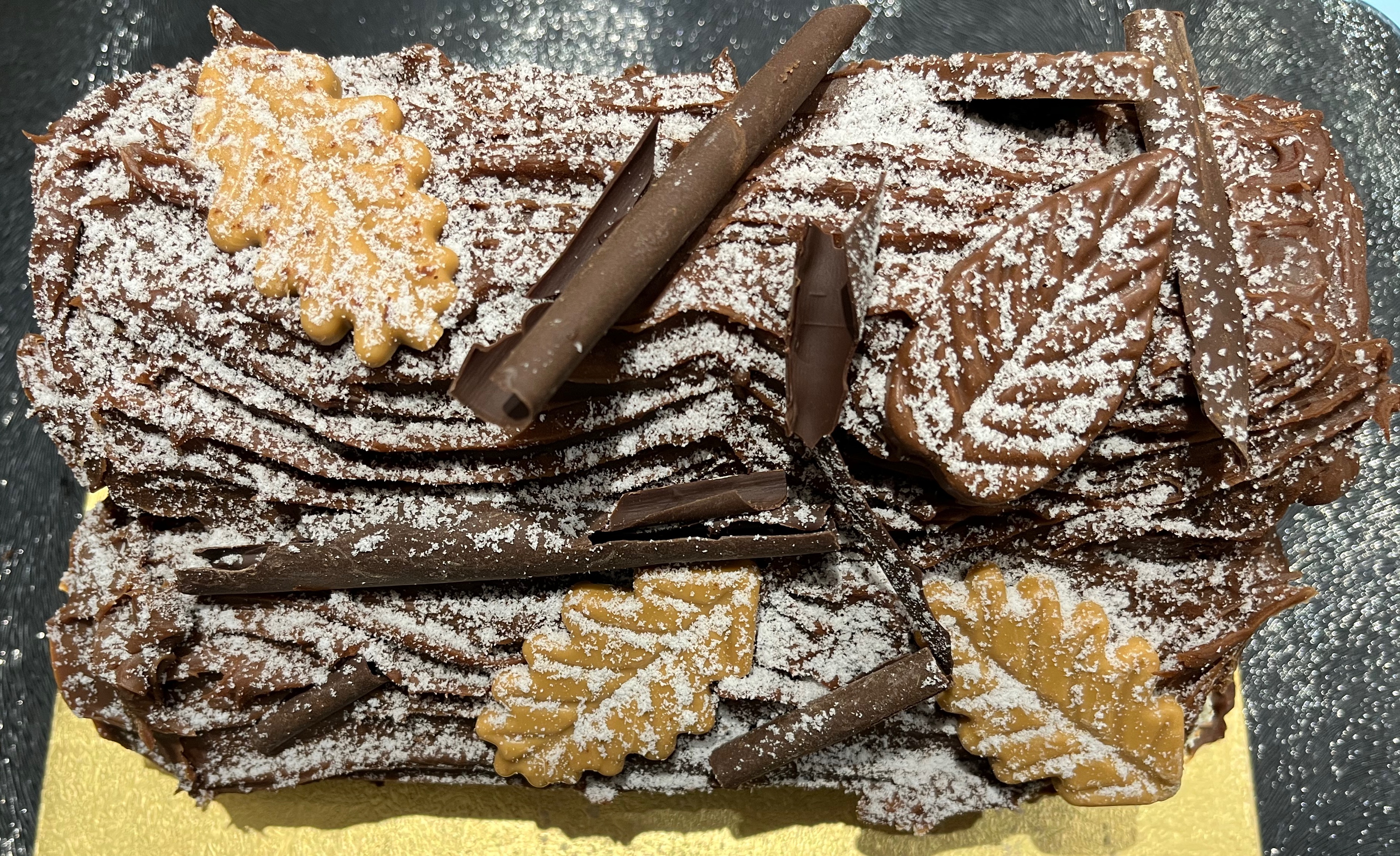 A large triple chocolate yule log from Marks and Spencer. It has the realistic appearance of a thick tree trunk, with edible decorations of leaves and twigs, all covered with a dusting of sugar like snow.