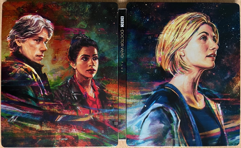 Cover spread for the Doctor Who Series 13 Blu-ray Steelbook, showing a colourful painted image of the Doctor and her companions Dan and Yaz.