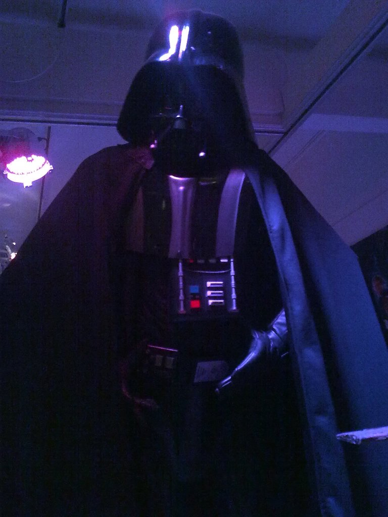 Life-size model of Darth Vader from Star WArs, the tall menacing figure wearing a black robe over black armour and a black helmet.
