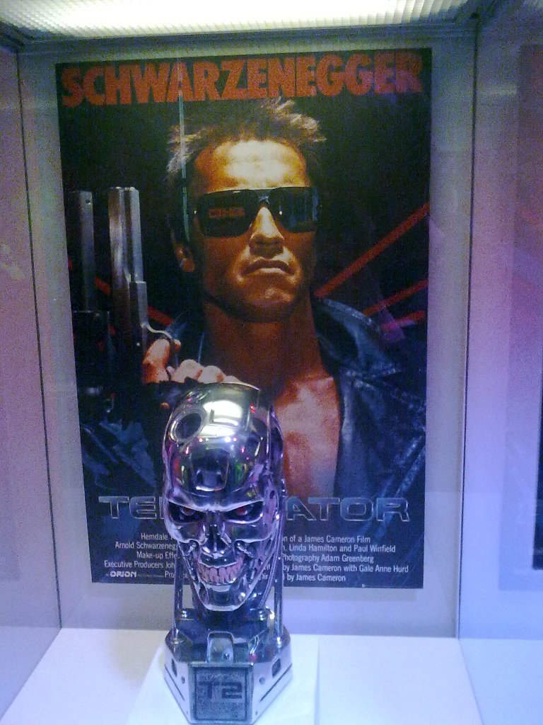 Model of the Terminator's evilly grinning robot head, in front of a poster showing Arnold Schwarzenegger playing the Terminator in the first film.