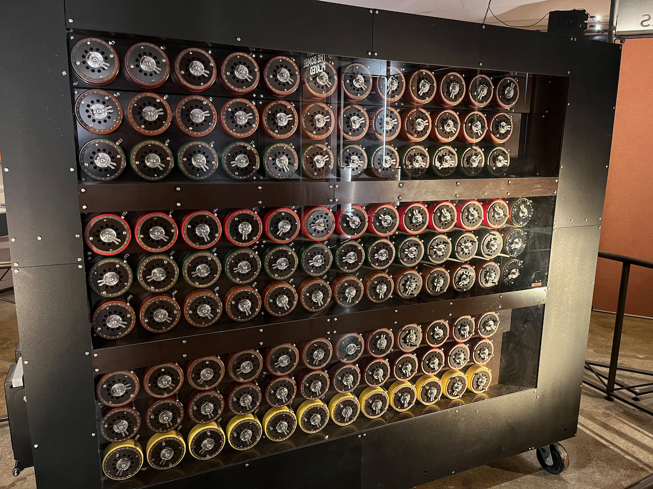 The Bombe machine, a large black cabinet in which there are 9 rows of 12 rotor wheels, divided into blocks of 3. Each wheel has 26 positions, one for each letter. The central block has an extra column of 3 wheels on its far right, which displays the final result of the current operation.