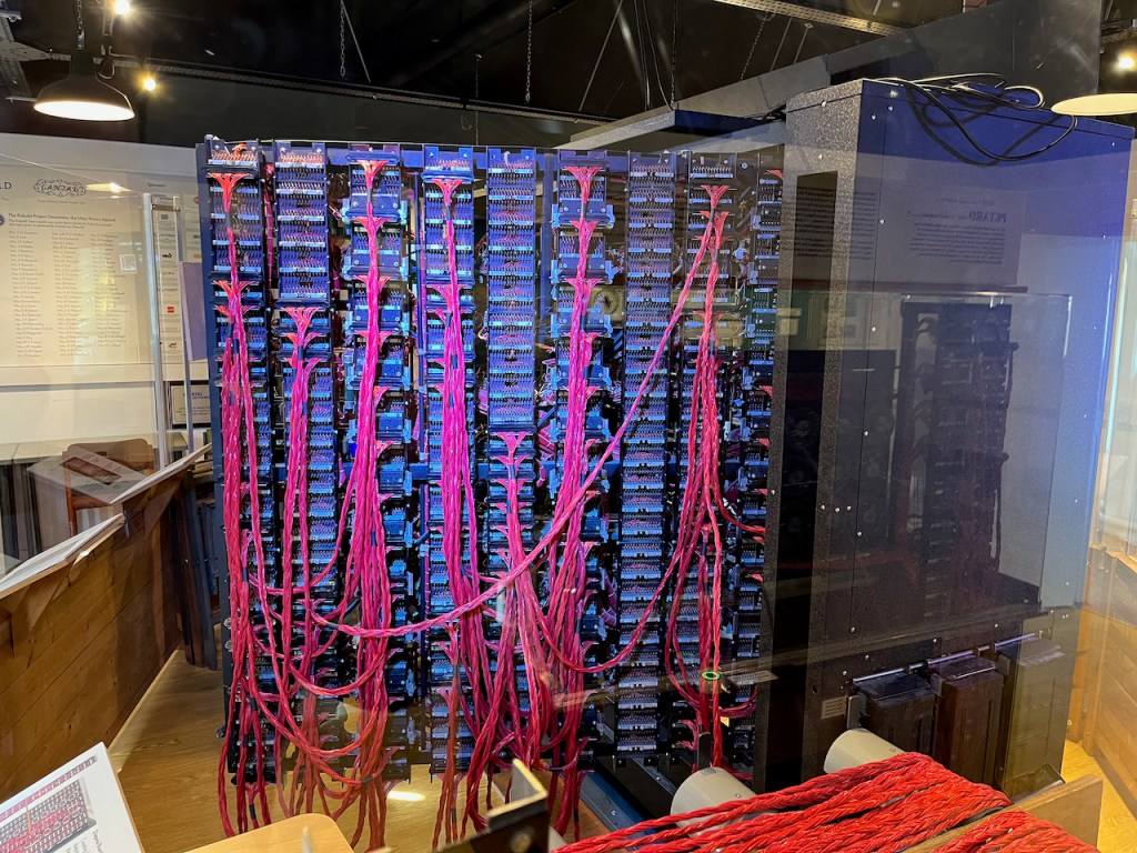 The back of a Bombe machine, showing 9 columns of complex sockets, with lots of long red cables sticking into many of them and criss-crossing each other.