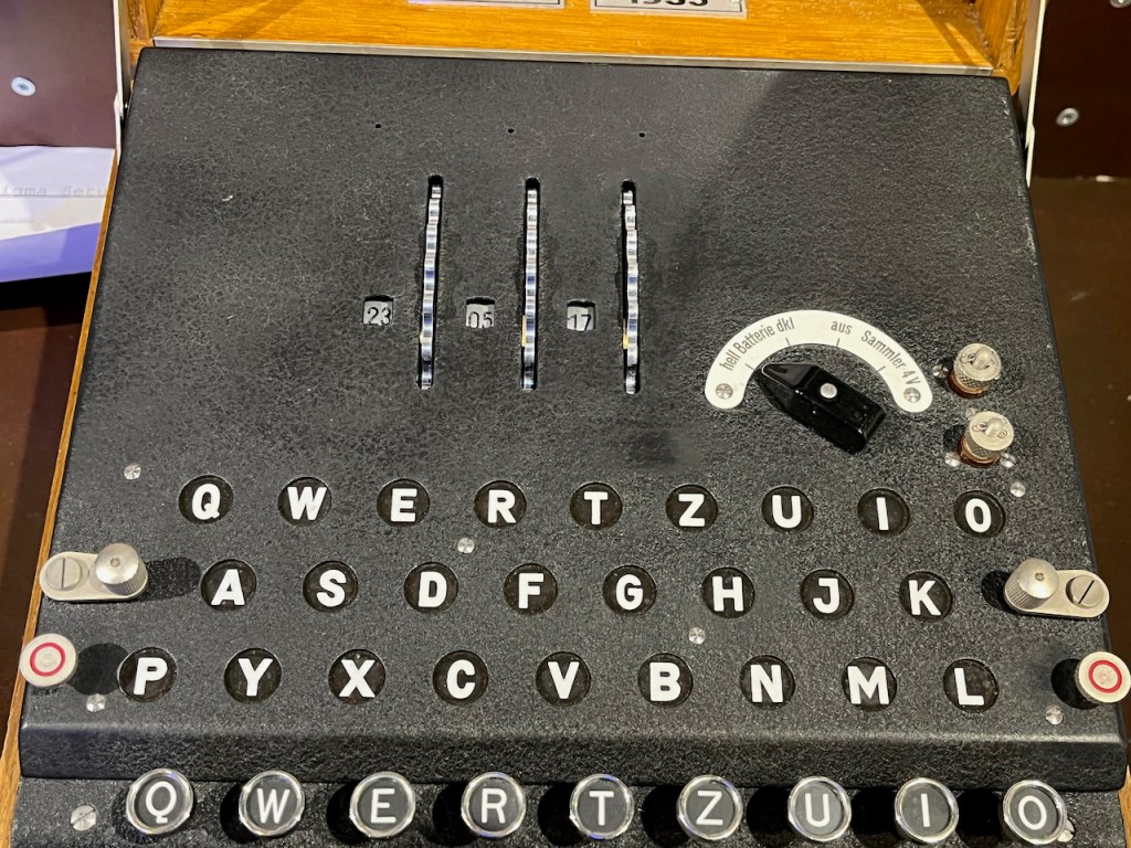 Close-up of the top of the Enigma machine, showing 3 embedded rotor wheels, with a tiny window next to each showing the current number it's been set to.