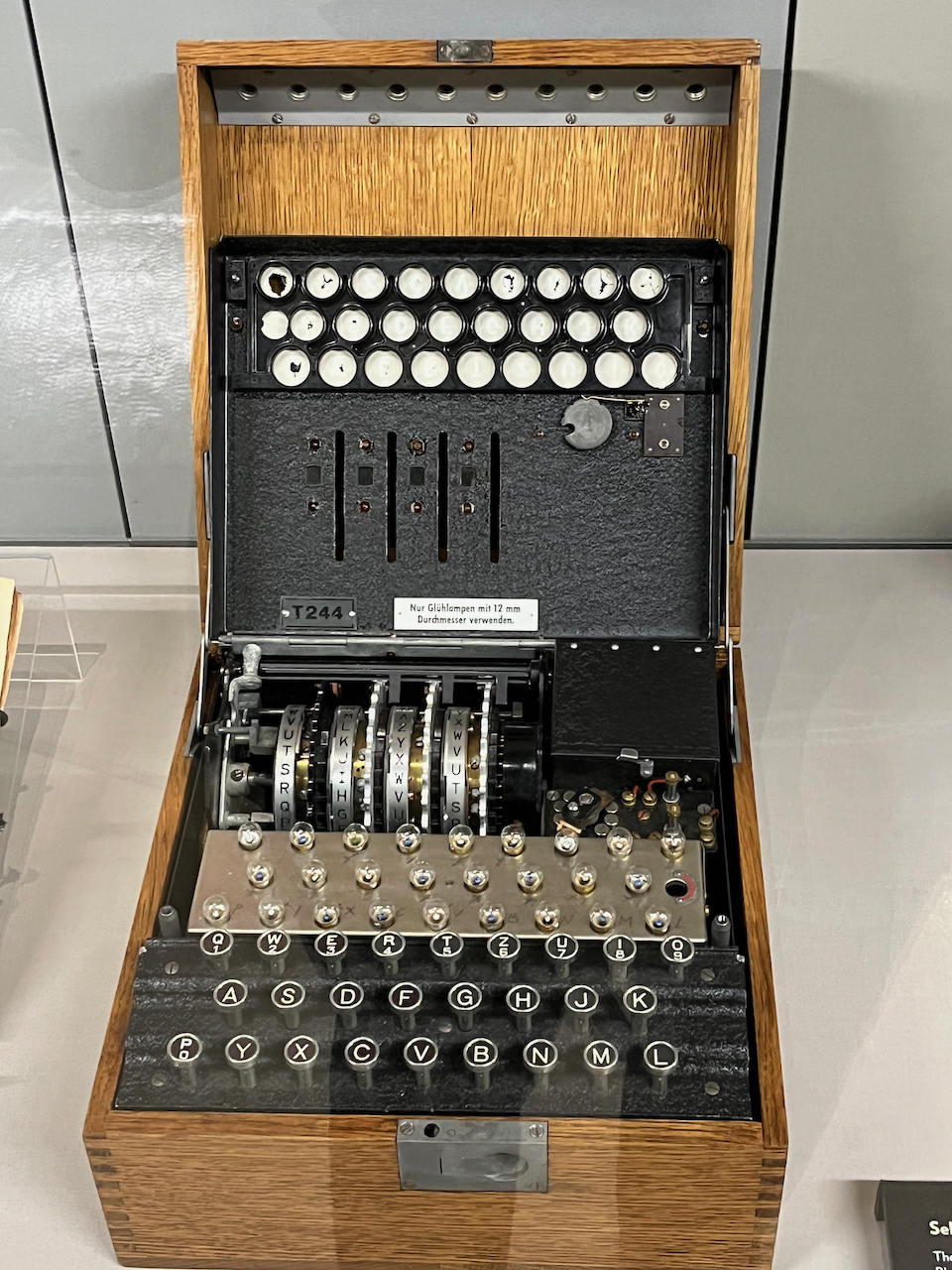 An Enigma machine with an inside panel lifted, so that we can see the individual lightbulbs between each of the coded letters that are lit when keys are pressed
