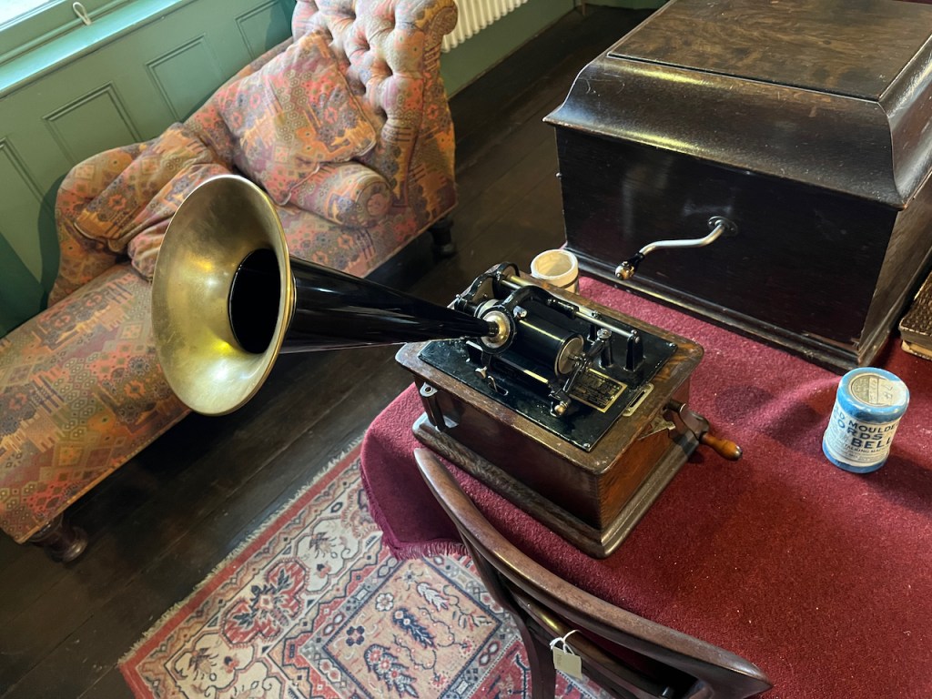 An old music player, consisting of a wooden box with a metal roll and other metal elements on top, and a large metal cone sticking diagonally upwards out of it to amplify the sound.