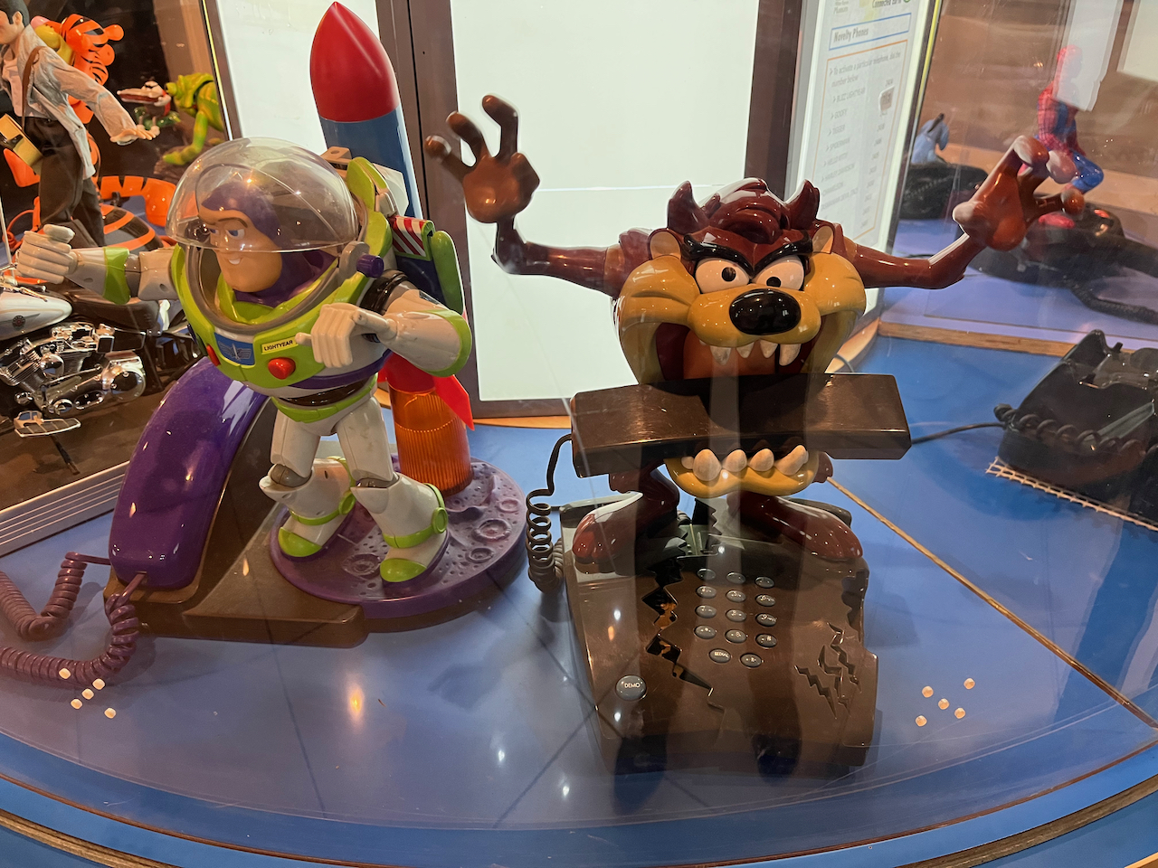 A couple of novelty phones. On the left, Toy Story astronaut Buzz Lightyear has a rocket strapped to his back, while the purple phone receiver sits beside him. To his right, another phone has the Tasmanian Devil raising his arms while holding the brown receiver between his sharp teeth.
