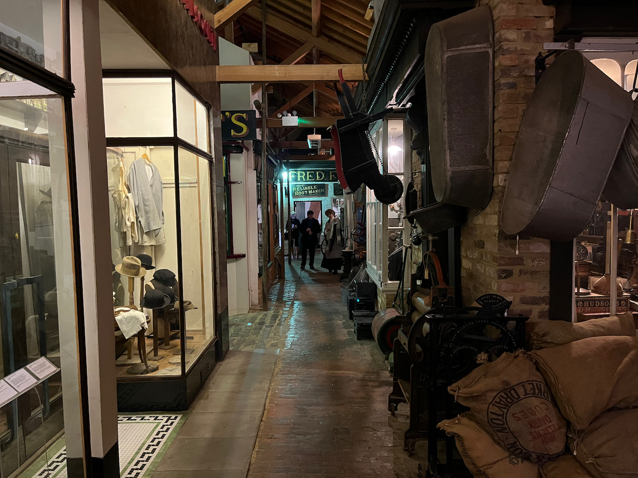 A recreation of an old street of shops. Viewed from one end to the other, the window of the shop nearest us contains some hats and shirts, while at the far end of the street is a boot maker.