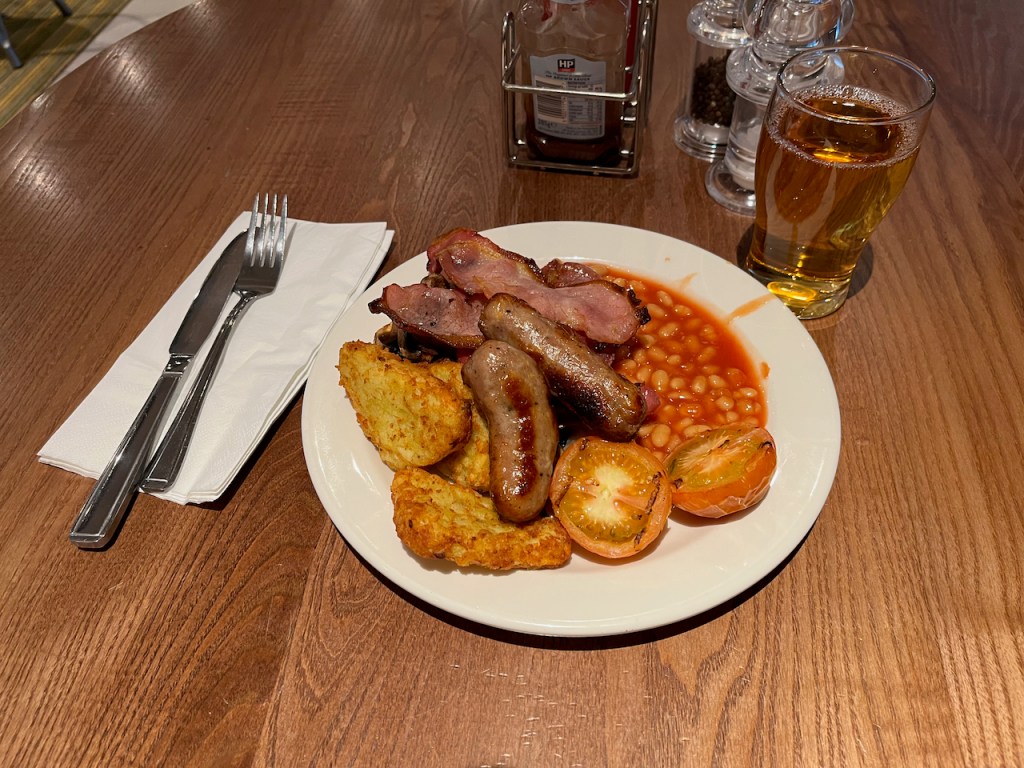 My Premier Inn breakfast, with bacon, sausages, baked beans, hash browns, tomatoes and mushrooms, accompanied by a glass of apple juice.