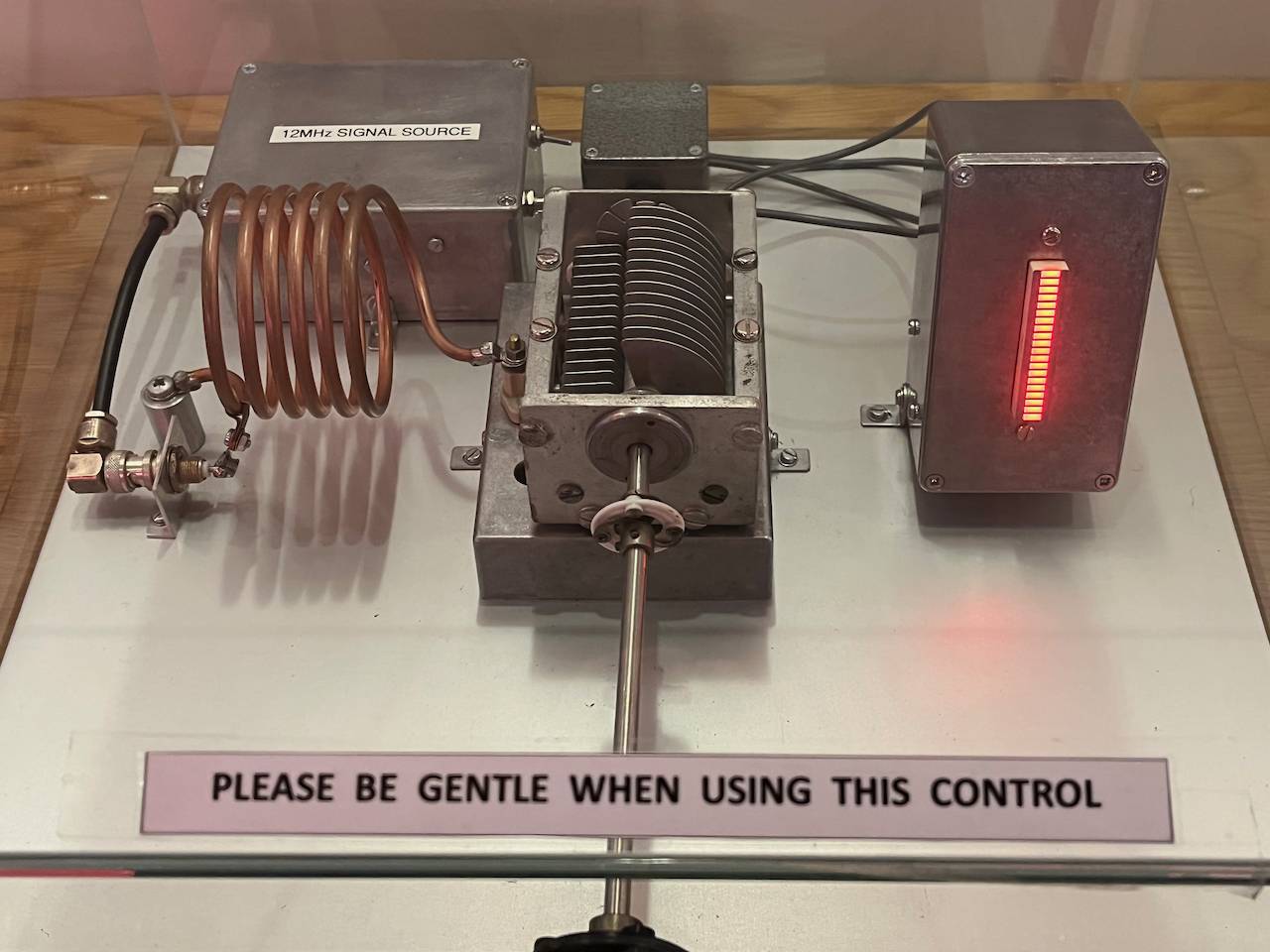 A tuning demonstration unit. Turning the dial brings two sets of metal teeth together in the middle, changing the current in the coiled wire to the left of them, and lighting up a thin display column in the small metal box on the right. 