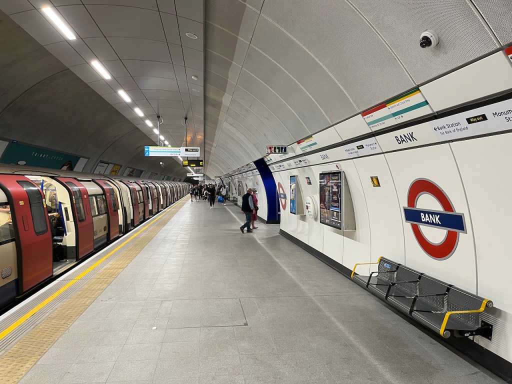 The new, wide southbound platform for the Northern Line at Bank. A large group of people are walking down from the far end, having just got off the train. They are spread out nicely, as the platform gives them plenty of room to do so.