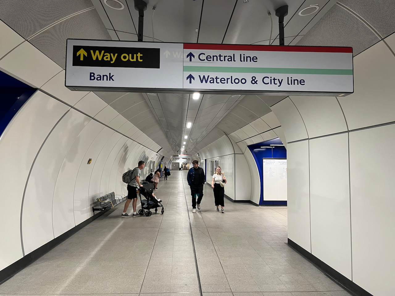 The new wide concourse for the Northern Line at Bank, formed from the old Southbound tunnel. The walls and floors are white, while the side tunnels to each platform have dark blue walls.