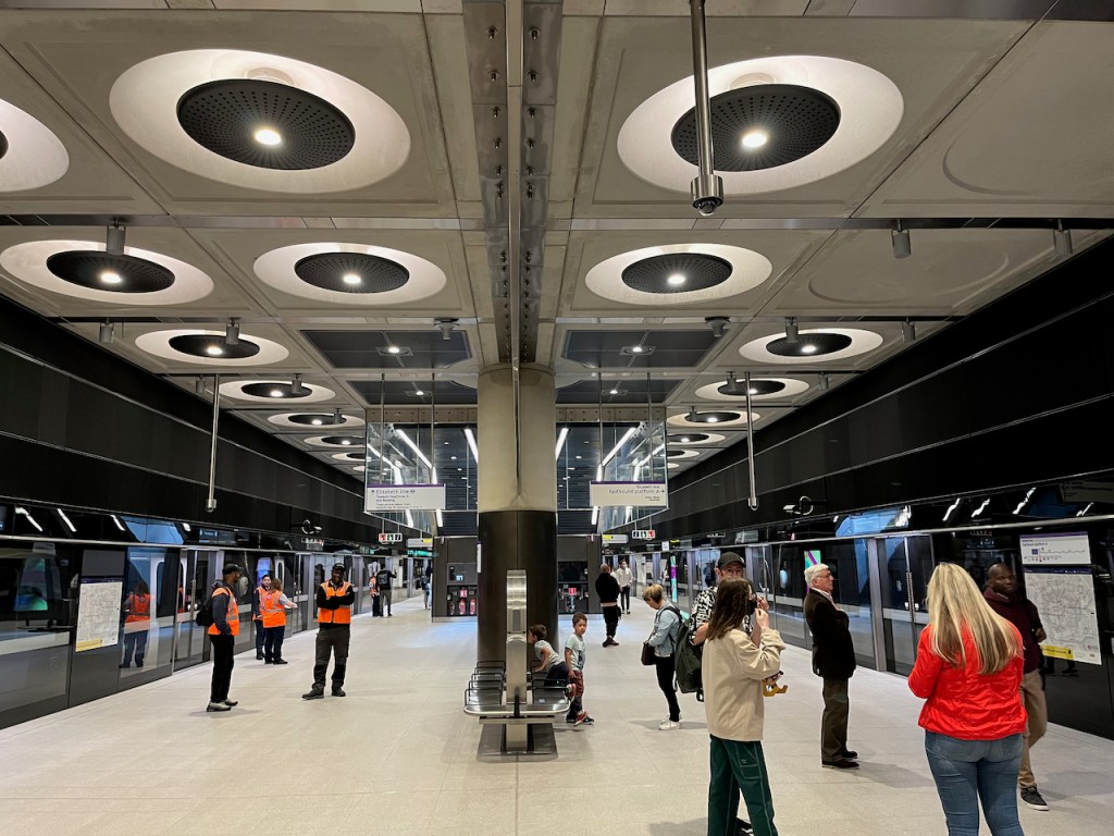 View between the 2 wide Elizabeth line platforms at Paddington, with big circular lights along the ceiling.