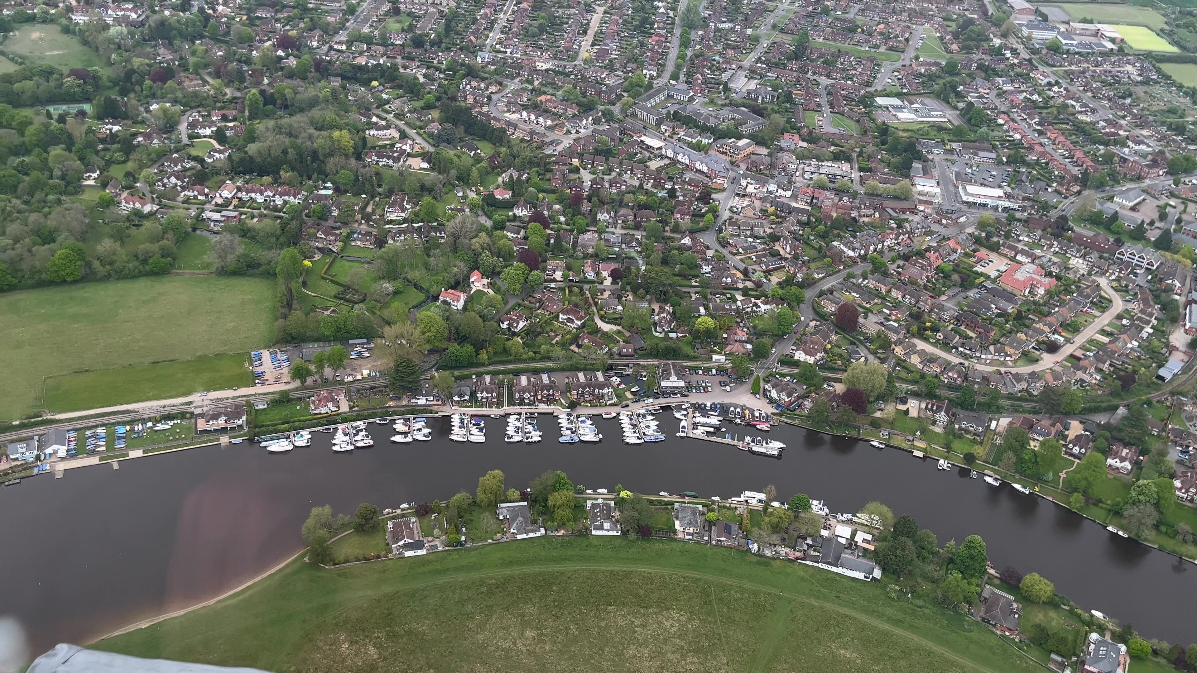 Helicopter view of lots of boats moored on a river next to some houses.