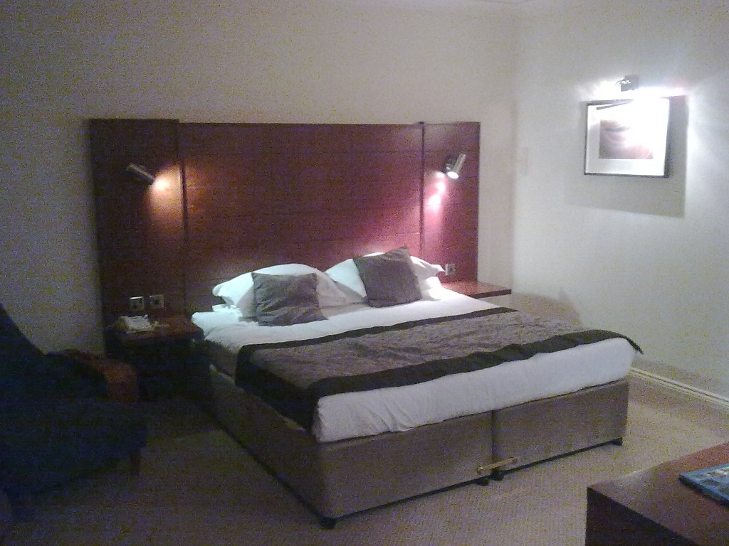 Double bed with a tall red heabin my Bristol hotel room, with a small cushion resting on each of the two pillows.