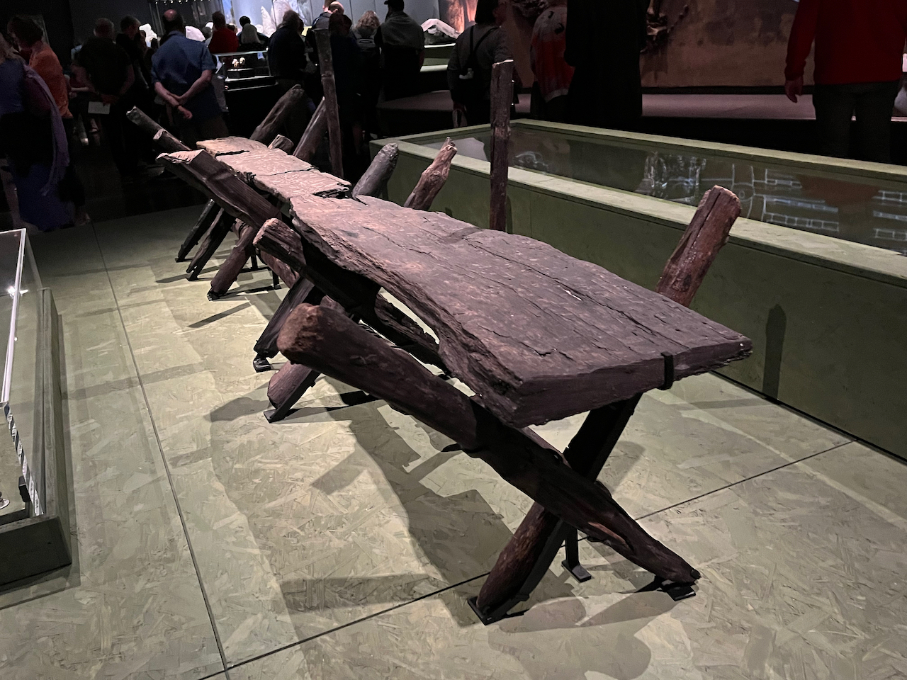 A long. thick, wooden walkway, held up by smaller logs of wood arranged in diagonally crossed pairs beneath it to support it.