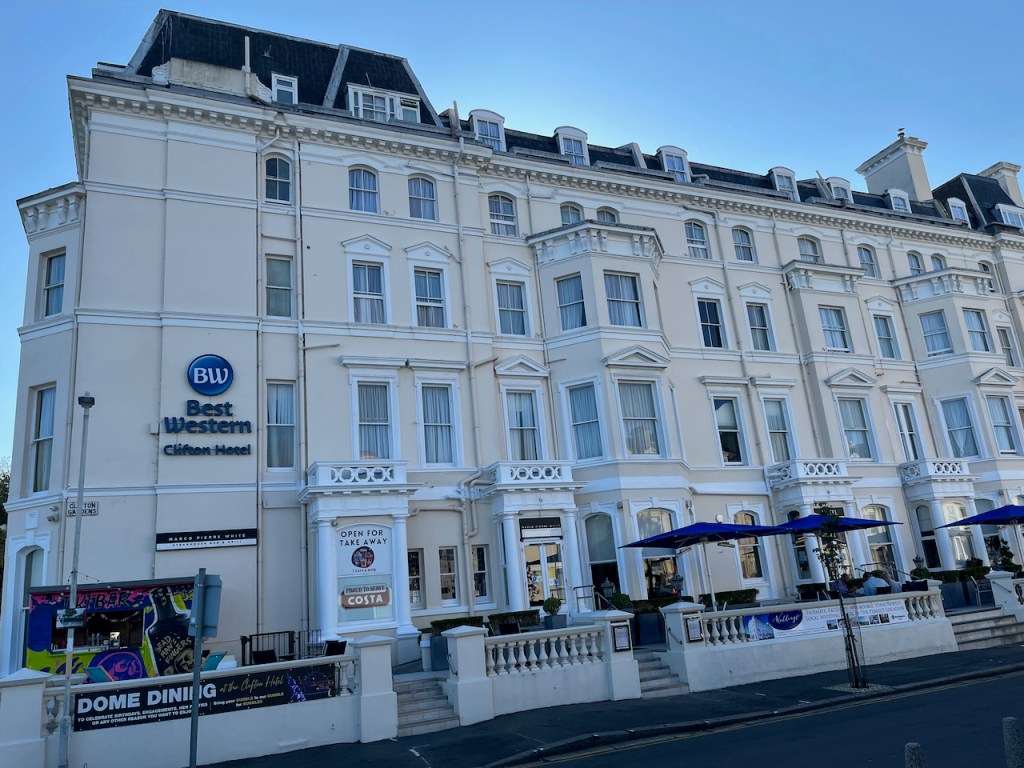 The exterior of the Best Western Clifton hotel, a large white 4-story building, with signs for the Marco Pierre White steakhouse restaurant and Costa takeaway on the ground floor.