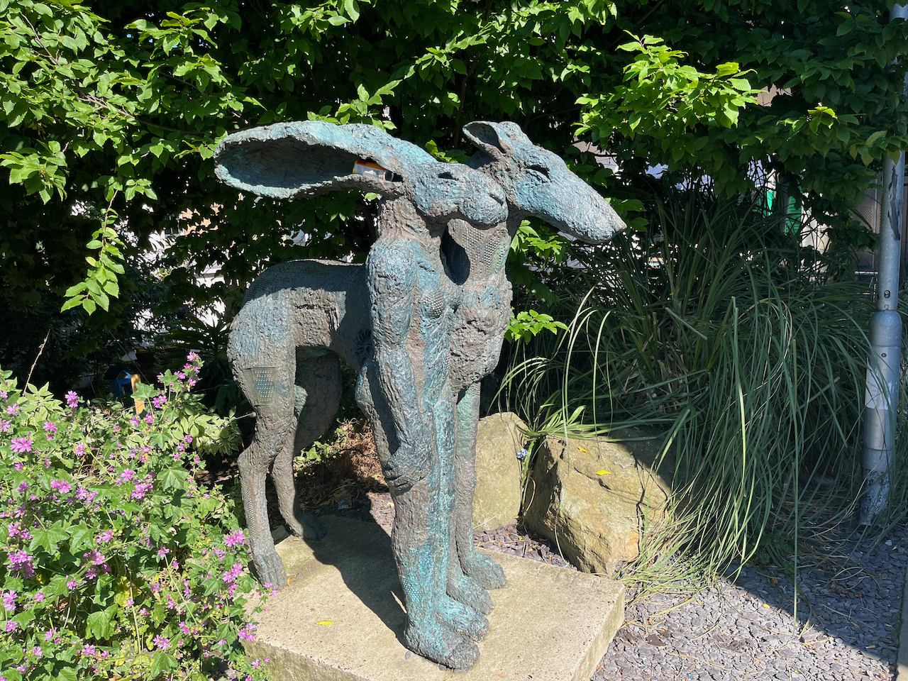 A statue of a hare standing next to a greyhound. This is an artwork called Standing Lady-Hare With Dog by Sophie Ryder.