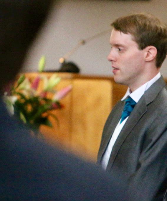 Glen as best man looking thoughtful during the wedding ceremony, with colourful flowers visible in the background.