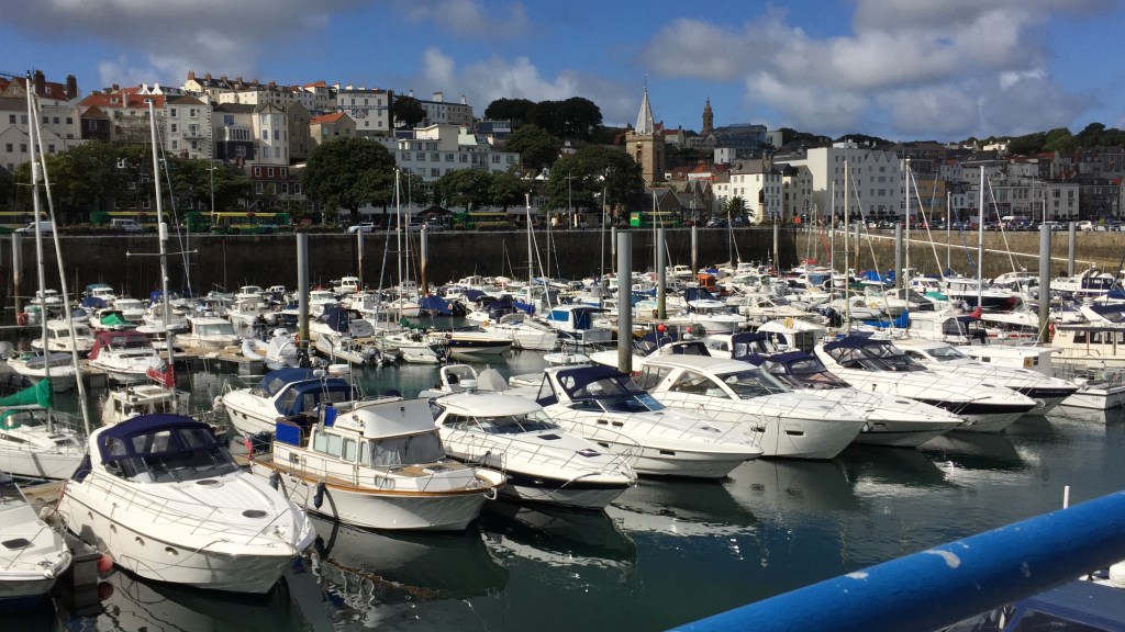 Lots of boats moored in Guernsey harbour, with lots of buildings up on the hills behind them.